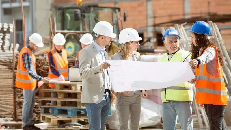 A group of construction professionals is discussing a blueprint at a construction site.