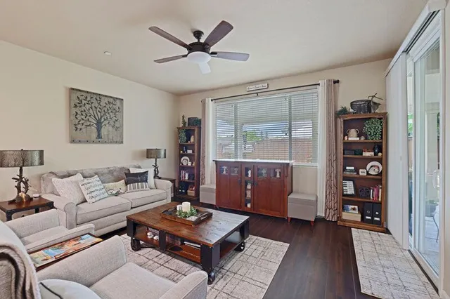 A living room featuring a gray sofa, two armchairs, a wooden coffee table, a ceiling fan, and two wooden bookshelves.